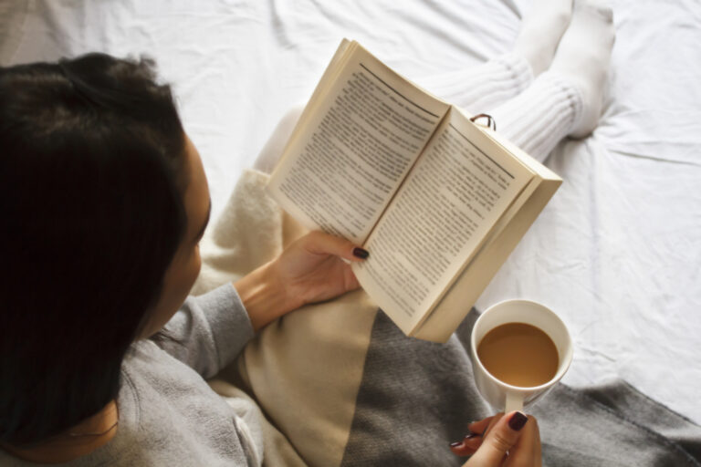 girl reading book and drinking coffee in bed in the morning
